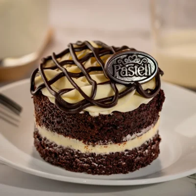 Versión individual y esponjosa de nuestro bizcocho de chocolate relleno de queso crema, cubierto con crema Pasteli y líneas de ganach de chocolate semiamargo. Repostería individual a domicilio en Chihuahua.